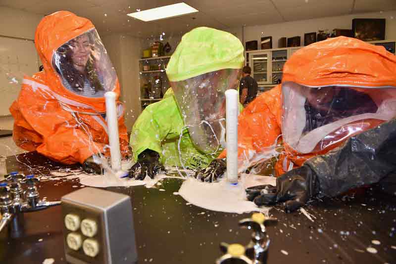 three high school students in a lab with exploding white foam