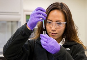A woman adds a liquid to a flask in a research setting