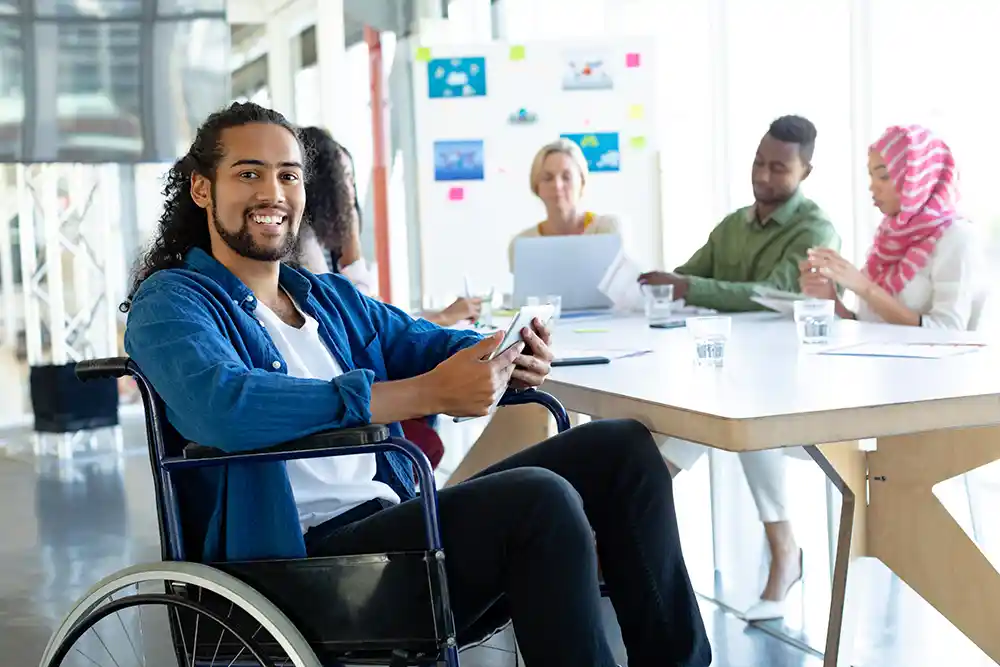 black man in wheelchair in office setting with other associates at a table