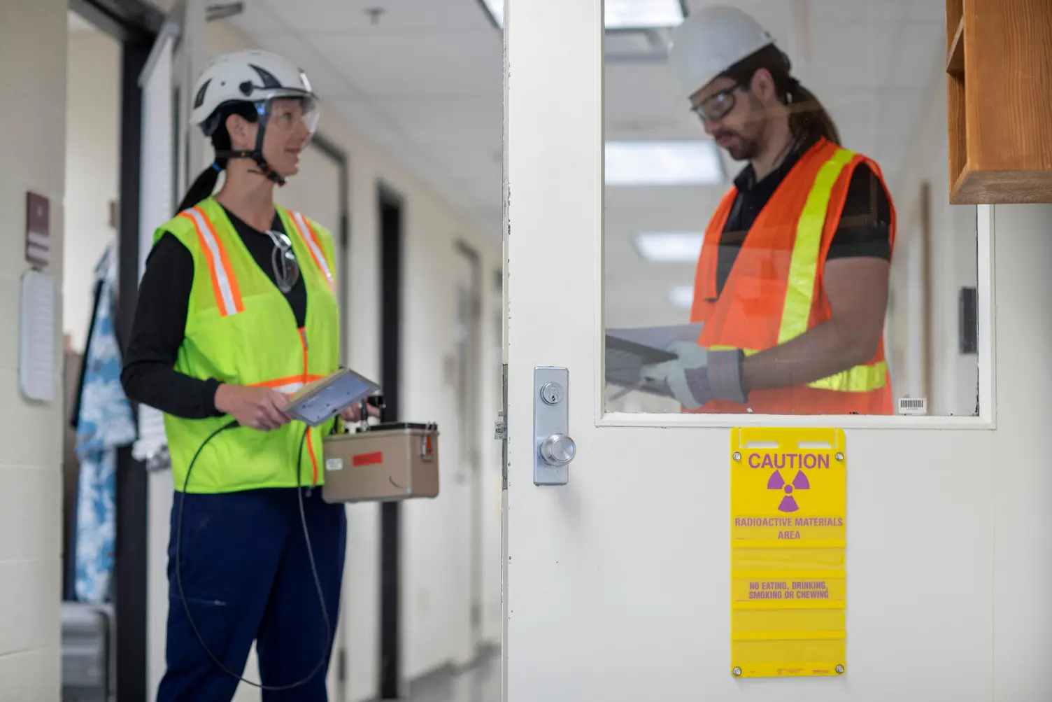 Two male technicians work in an area with hazardous signage