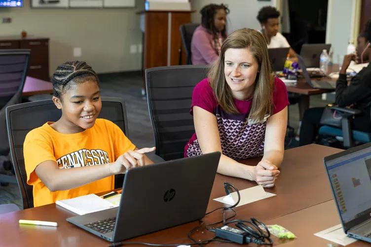 A student and teacher discuss an assignment while using a laptop computer