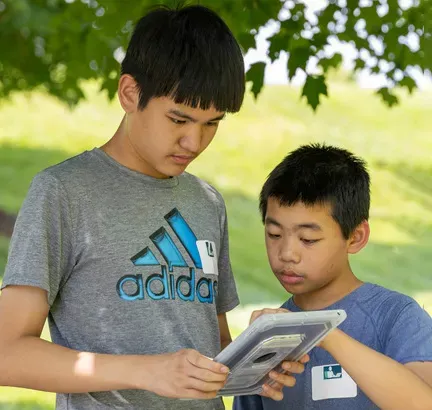 Two students work together outdoors using a tablet to complete an assignment