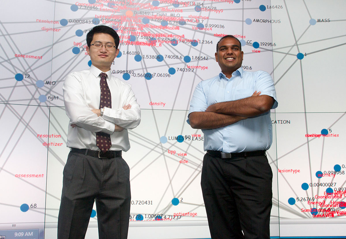 Two postdoctoral fellows in front of data visualization wall